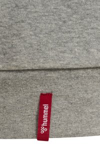 Szara bluza z gładkiego materiału. Zawiera czerwony metek z białym napisem "hummel" wszyty w dół. Prosty wzór.