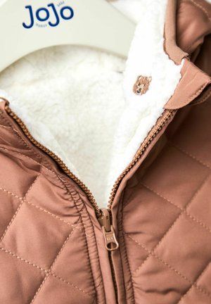 Barna steppelt dzseki krémszínű, bolyhos béléssel, fém cipzárral és medve emblémával a gallérnál. Egy fehér vállfán lóg.