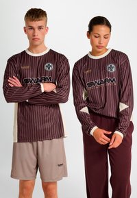 Langärmelige bordeauxrote gestreifte Trikots mit cremefarbenen Akzenten und einem Logo, kombiniert mit beigen Shorts. Glatter Stoff mit sportlicher Passform.