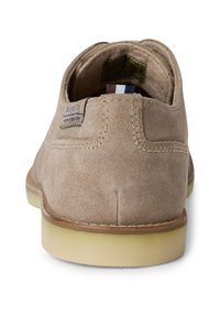 Chaussure en suede beige clair avec un bout arrondi, semelle blanche et coutures visibles. Présente une étiquette de marque au talon et une doublure intérieure lisse.