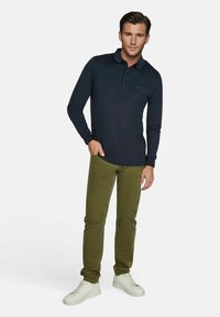 Navyfarbendes Langarm-Polohemd mit Brusttasche, kombiniert mit olivgrünen, schmal geschnittenen Hosen und weißen Sneakern. Lässige Kleidung mit schlichtem Design.