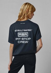 Musta puuvilla t-paita, jonka selässä on valkoisella painettuna "RED BULL RACING" ja "PIT STOP CREW", lyhyet hihat käännettävillä reunuksilla ja rento istuvuus.