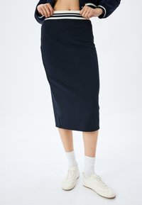 Jupe midi bleu marine en tissu extensible, avec une taille à rayures blanches contrastantes. Conçue avec une silhouette ajustée et des fentes sur les côtés.