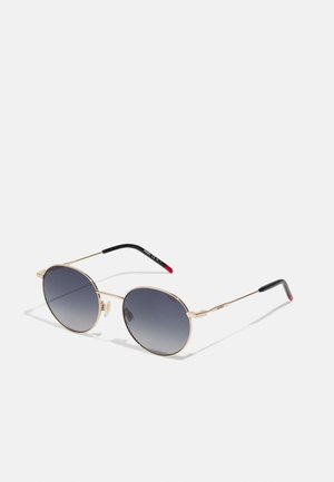 Ochelari de soare cu ramă din metal aurit, cu lentile întunecate cu gradient, de formă rotundă, și vârfuri negre cu accente roșii pe brațe.