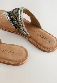 Sandali con perline, con una soletta in suede marrone, accenti argentati e un design di perline multicolore sulla cinghia, caratterizzati da uno stile a infradito e una suola piatta.