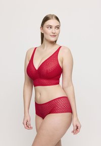 Bralette in pizzo rosso con spalline regolabili, caratterizzata da una forma triangolare e una fascia sottostante spessa, abbinata a slip hipster in pizzo coordinati.