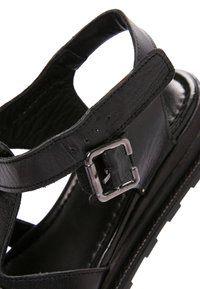 Sandaletto in pelle nera con cinturino regolabile con fibbia argentata e suola texturizzata, vista ravvicinata angolata.