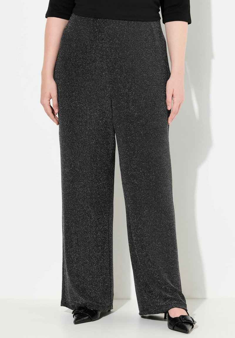Pantalons larges noirs avec une texture chatoyante, dotés d'une taille élastique et d'une finition en tissu lisse. Associés à des chaussures noires.