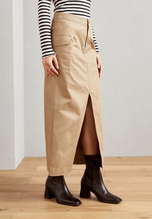 Beige bomull midi skjørt med slit i front, sidelommer og tettsittende midje. Kombinert med svarte ankelstøvler med firkantet tå.