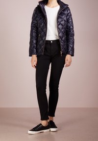 Vadderad marinblå pufferjacka med huva, i ett glänsande material, med dragkedjefickor och bruna detaljer, kombinerad med svarta jeans och svarta sneakers.