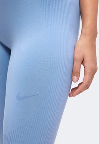 Gros plan sur la cuisse et la main d'une personne portant un legging bleu clair texturé avec un logo Nike discret près du haut de la cuisse.