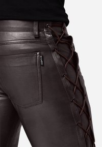 Bruine leren broek met een gespsluiting aan de zijkant en een bruine koord. Inclusief een achterzak met een zwart label. Gladde textuur.