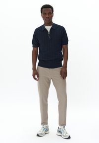 Námornícky pletený polokošeľa so zipsom, kombinovaný s béžovými slim-fit nohavicami a šedými teniskami s modrými akcentami. Minimalistický dizajn, ležérny strih.