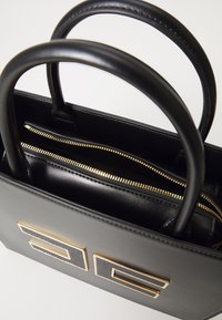 Black leather handbag with gold hardware, featuring two handles and a zippered pocket inside. Notable design includes embossed accents.