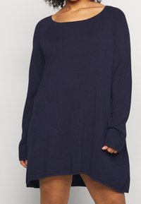 Marineblauwe lange mouw tuniek met een brede halslijn, zachte stof, een ontspannen pasvorm en een hoge-lage zoom die visuele interesse toevoegt.