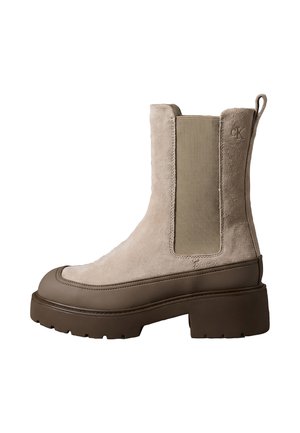 Bota Chelsea beige de ante de altura media con suela gruesa marrón oscuro, panel lateral elástico, lengüeta y logotipo CK en relieve en el lado exterior.