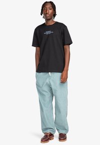 Black cotton t-shirt with blue "ELEMENT SKATEBOARD CO. WORLD WIDE" text, paired with light blue baggy pants and brown shoes.