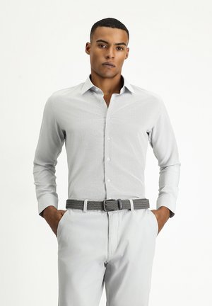 Camisa de manga larga gris claro con una textura sutil, frente abotonado y cuello, combinada con un cinturón trenzado gris. Pantalones en un tono claro a juego.