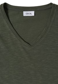 T-shirt vert olive à col en V avec une étiquette blanche affichant le nom de la marque CECIL cousue dans l'encolure.