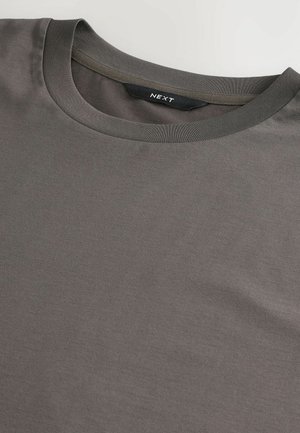 T-shirt en coton gris avec un col rond, présentant un design simple et une texture lisse. L'étiquette de la marque 'NEXT' est visible à l'intérieur du col.
