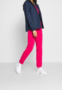 Granatowa lekka kurtka z kapturem noszona na jasnoróżowej bluzce, w zestawieniu z różowymi spodniami i białymi wysokimi trampkami.