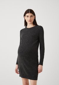 Fekete kismama ruha hosszú ujjakkal, kerek nyakkiv�ágással, texturált kötött anyagból, és fitt sziluettel, amely kiemeli a terhes alakot.