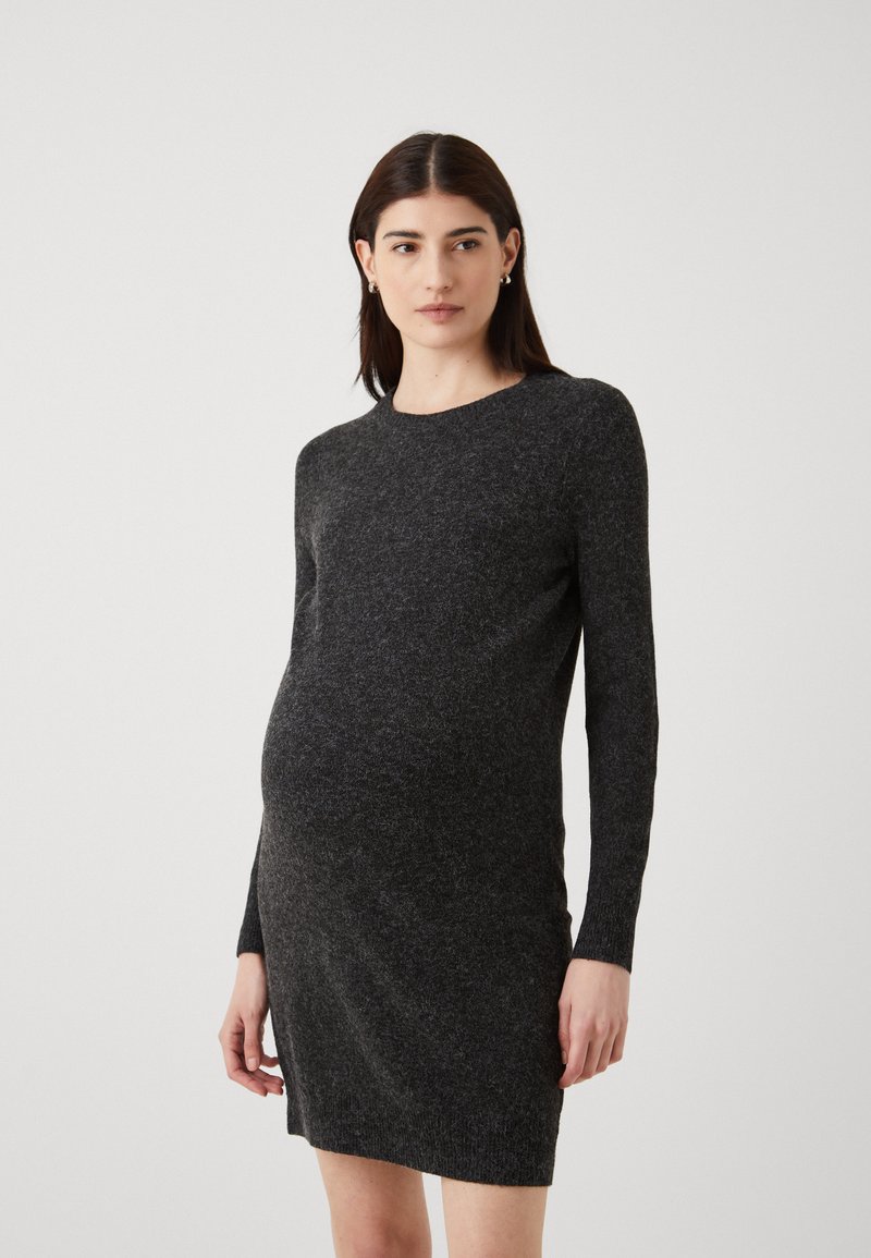 Fekete kismama ruha hosszú ujjakkal, kerek nyakkivágással, texturált kötött anyagból, és fitt sziluettel, amely kiemeli a terhes alakot.