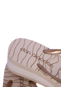 Chanclas beige con un patrón texturizado ondulado, con correas metálicas marrones y un acento blanco en la suela. Etiqueta de la marca visible.