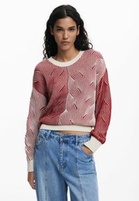 Rot-weiß gemusterter Pullover mit Rundhalsausschnitt, langen Ärmeln und gerippten Bündchen. Kombiniert mit hoch taillierten blauen Jeans.