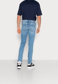 Ljust blå denimjeans med smal passform, med medelhög midja, bakfickor och vit sömnad. Bärs med svart- och vitfärgade sneakers.