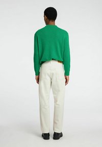 Maglione verde a maglia con collo rotondo, abbinato a pantaloni bianchi a gamba dritta. L'outfit presenta una vestibilità comoda e un design minimalista.