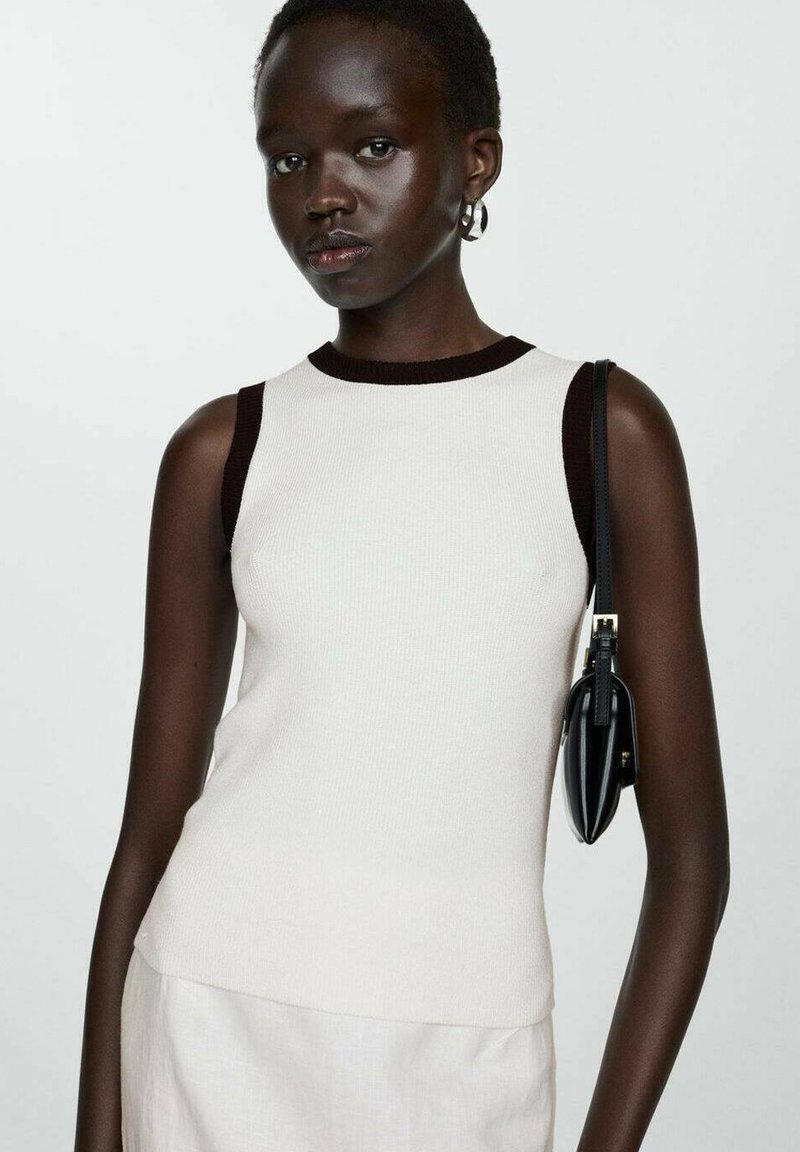 Cream sleeveless top with a ribbed texture, dark brown trim along the neckline and armholes, paired with a small black handbag.