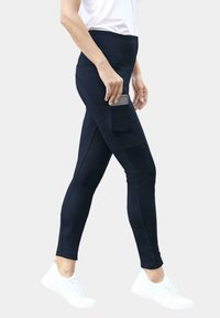 Leggings navy avec une taille haute, poche latérale, texture lisse et forme ajustée, associés à des chaussures de sport blanches.