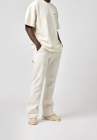 T-shirt en coton beige à coupe ample et manches courtes, associé à un pantalon en coton beige avec poches latérales et une coupe droite.