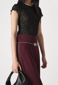 Czarny koronkowy top z krótkimi rękawami, połączony z buraczkowymi spodniami z wysokim stanem, które mają srebrny pasek oraz czarną torebkę.