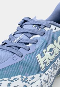 Basket de sport bleu clair avec une tige texturée, des accents à motif, des lacets plats et une semelle blanche éclaboussée. Affiche le nom de la marque "HOKA" de manière proéminente.