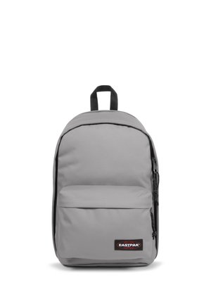Mochila de color gris claro con un bolsillo frontal, cordones negros en la cremallera, asa superior negra y un parche con el logo de Eastpak en rojo y blanco en el bolsillo.