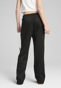 Svarta sweatpants med avslappnad passform, med vita sidostripes, elastisk midja och slät tygtextur.