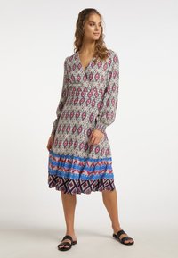 Rochie cu mâneci lungi, cu un model, având un decolteu adânc în V, talie elastică și un tiv voluminos în nuanțe de roz, albastru și alb pe un fundal gri.