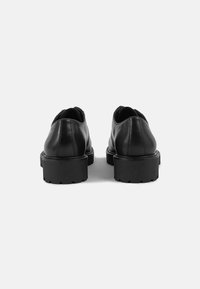 Sapatos de couro preto com um design arredondado, solas grossas em borracha preta e uma textura suave. Apresentam uma costura subtil ao longo da parte de trás.