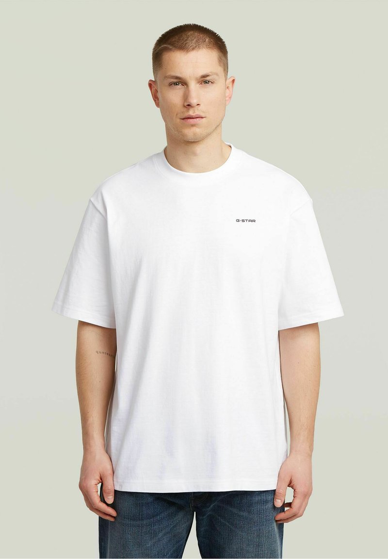 Camiseta de algodón blanca con escote redondo, mangas cortas y un pequeño logo negro "G-STAR" en el pecho. Combinada con jeans de mezclilla azul.