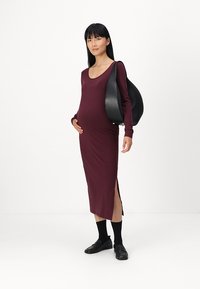 Sötét bordó anyagú kismama ruha, testhez sima, hosszú ujjú és oldalsó hasítékokkal; fekete bőrtáskával és fekete cipőkkel párosítva.