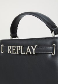Sac en cuir noir au design simple, avec un accent en argent "REPLAY" et une finition lisse et texturée.