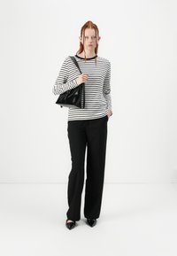 Top de manga larga a rayas en blanco y negro combinado con pantalones negros de pierna ancha. La modelo sostiene un pequeño bolso de cuero negro. Zapatos negros de punta.