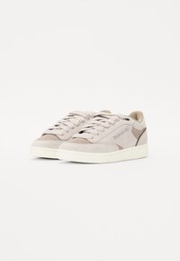 Light gray suede sneakers with a rounded toe, flat laces, and a textured white rubber sole. Features subtle branding and green accents.