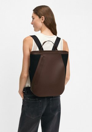 Brown leather backpack with a sleek design, mesh side panels, and wide black straps. Rounded shape with a top handle for easy carrying.