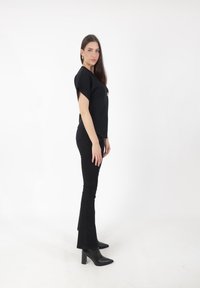 Schwarzes Kurzarmoberteil mit Rundhalsausschnitt, kombiniert mit hoch taillierten schwarzen Schlagjeans und schwarzen spitzen Knöchelstiefeln.