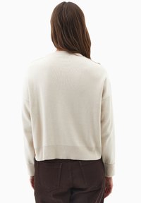 Maglione color crema con vestibilità rilassata, polsini e orlo a costine. Presenta un dettaglio in bottone dorato sulla spalla sinistra e una texture morbida.