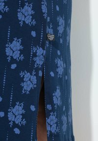 Indumento blu navy con motivo floreale in azzurro chiaro, caratterizzato da uno spacco laterale e da un piccolo etichetta nera. Realizzato in tessuto morbido e testurizzato.