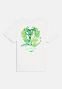 Balta medvilnė marškinėliai su žalia trofėjaus, teniso raketės ir kamuoliuko grafika, su užrašu "Saint-Tropez čempionatas 1986".